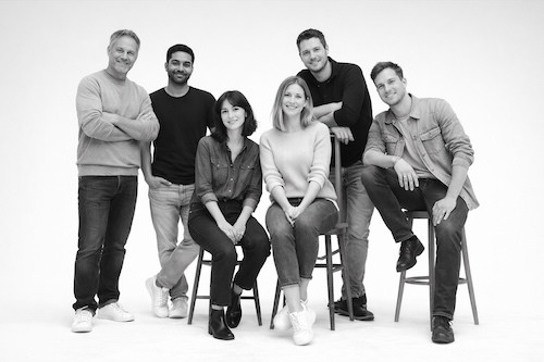 Group photo of six people in casual attire, sitting and standing on stools against a white background.