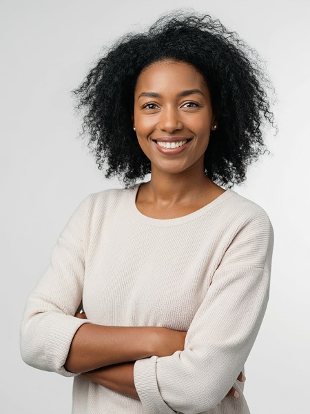 A woman with curly hair smiling, wearing a white sweater, with arms crossed against a light background.